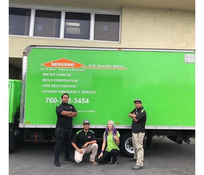 Three men and a lady standing in front of a green work truck.