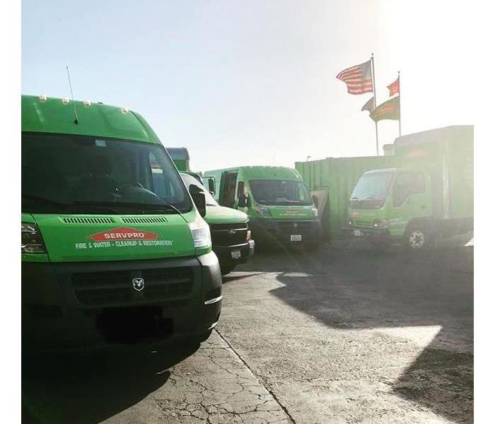 Green trucks in parking lot with flags in the background.